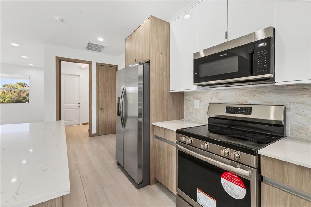 A modern kitchen features stainless steel appliances, light wood cabinetry, and white quartz countertops — 405 SUNSET ROAD N, ROTONDA WEST, FL