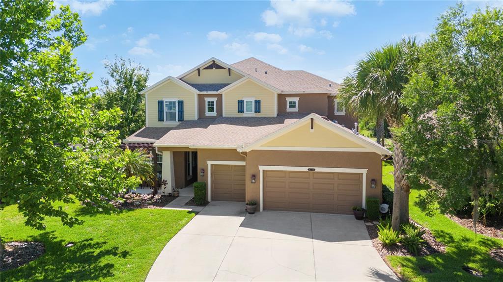 A two-story suburban house with a tan stucco exterior, a multi-car garage, and green landscaping — 8791 BELLA VITA CIRCLE, LAND O LAKES, FL