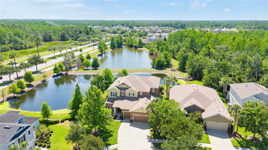 An aerial view shows a suburban house with a multi-car garage near a pond — 8791 BELLA VITA CIRCLE, LAND O LAKES, FL
