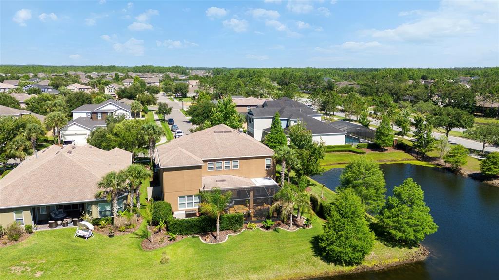 An aerial view shows suburban houses with screened lanais situated next to a small lake — 8791 BELLA VITA CIRCLE, LAND O LAKES, FL