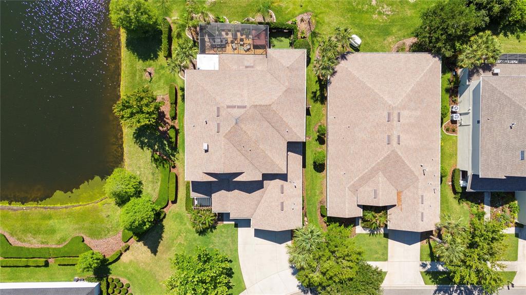 An aerial view shows two suburban houses with shingled roofs, driveways, and a nearby pond — 8791 BELLA VITA CIRCLE, LAND O LAKES, FL