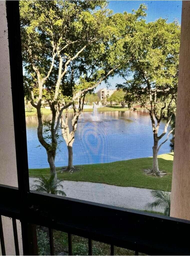 A view of a pond with a fountain framed by trees from a screened balcony — 955 Dotterel Road # 2309, Delray Beach FL 33444, DELRAY BEACH, FL