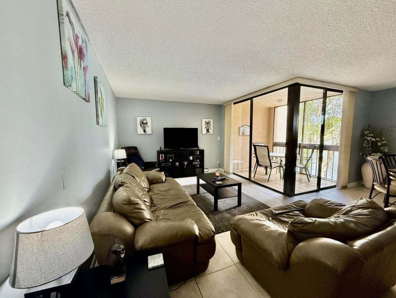 A living room features brown leather furniture, a television console, and a glass-enclosed balcony — 955 Dotterel Road # 2309, Delray Beach FL 33444, DELRAY BEACH, FL
