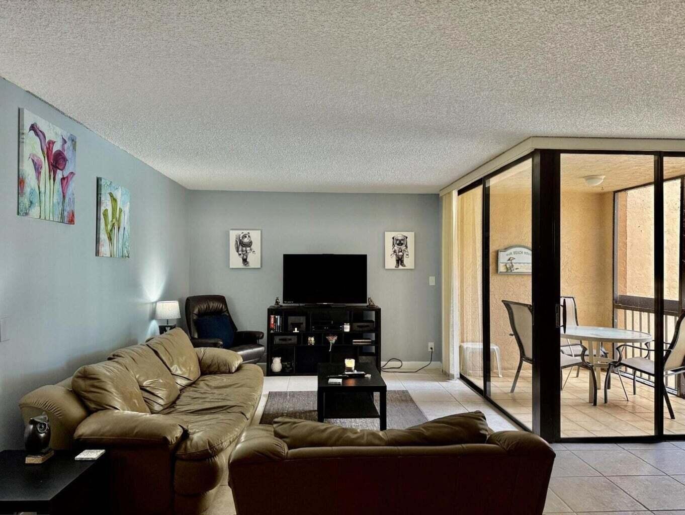 A living room with a leather sofa, television console, and sliding doors leading to a balcony — 955 Dotterel Road # 2309, Delray Beach FL 33444, DELRAY BEACH, FL