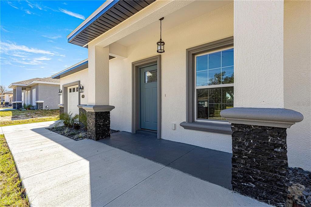 A covered front porch with a blue door, stone pillars, and a concrete walkway — 15201 SE 61ST COURT, SUMMERFIELD, FL