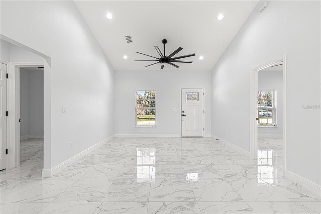 A bright, empty room features white marble-look tile flooring, a vaulted ceiling, and a ceiling fan — 15201 SE 61ST COURT, SUMMERFIELD, FL