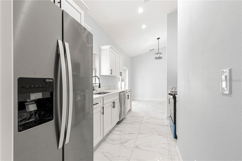 A kitchen features white cabinets, stainless steel appliances, and light-colored tile flooring — 15201 SE 61ST COURT, SUMMERFIELD, FL