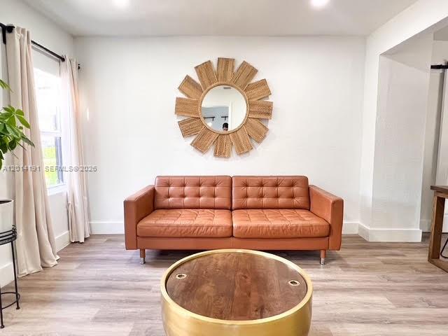 A living room features a tan leather sofa, a round coffee table, and a sunburst mirror — 1025 NW 55th St, Miami FL 33127, MIAMI, FL