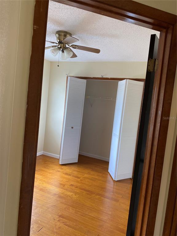 A bedroom features wood-look flooring, a ceiling fan, and a closet with white bifold doors — 7415 RADIANT CIRCLE, ORLANDO, FL