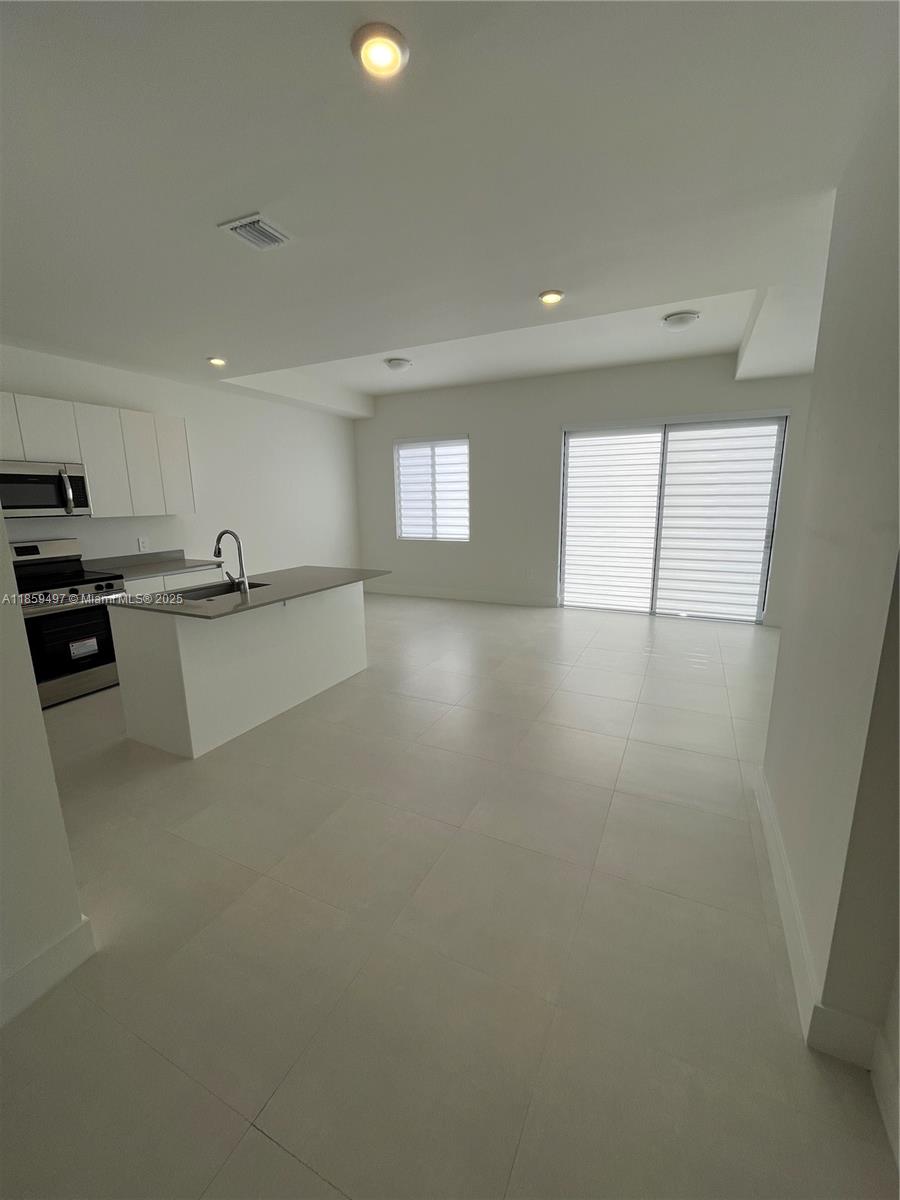A modern kitchen with white cabinets and a center island opens into a living area — 34515 SW 191st Ct, Miami FL 33034, MIAMI, FL