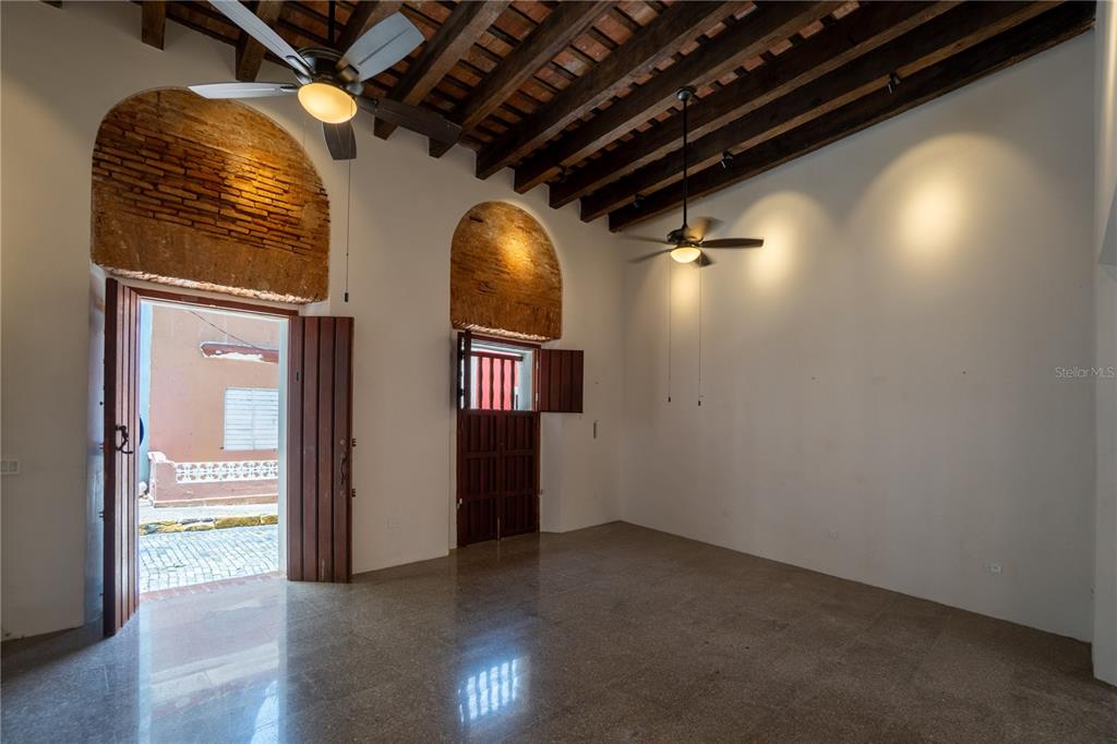 An interior room features exposed wood ceiling beams, arched brick accents, and polished stone floors — 8 DE LA CRUZ, SAN JUAN, PR