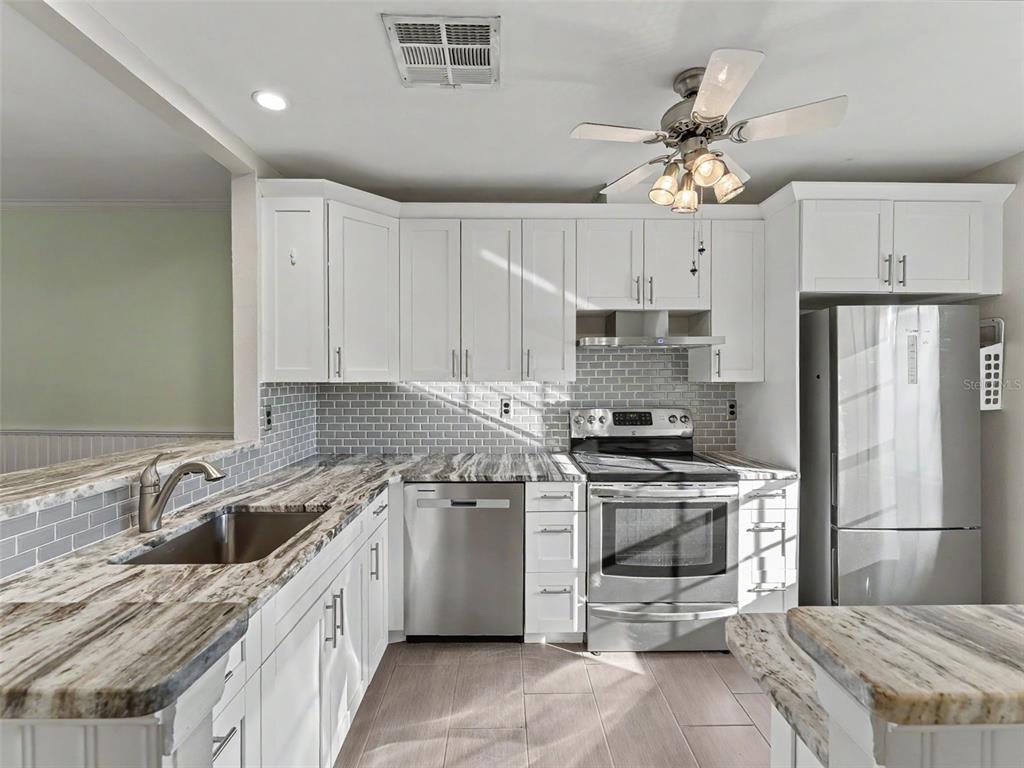 A kitchen features white cabinets, stainless steel appliances, and gray marble-patterned countertops — 11430 CARRIAGE HILL DRIVE UNIT 4, PORT RICHEY, FL