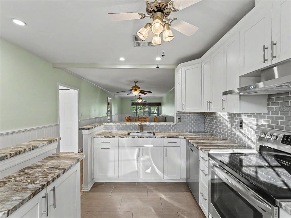 A kitchen with white cabinets, granite countertops, gray subway tile backsplash, and a ceiling fan — 11430 CARRIAGE HILL DRIVE UNIT 4, PORT RICHEY, FL