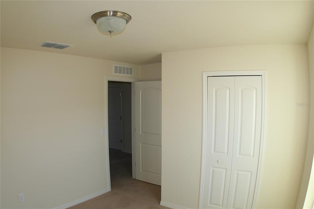 A bedroom features beige walls, carpeted flooring, a ceiling light fixture, and a white closet — 4362 HIGH RIDGE AVENUE, SPRING HILL, FL