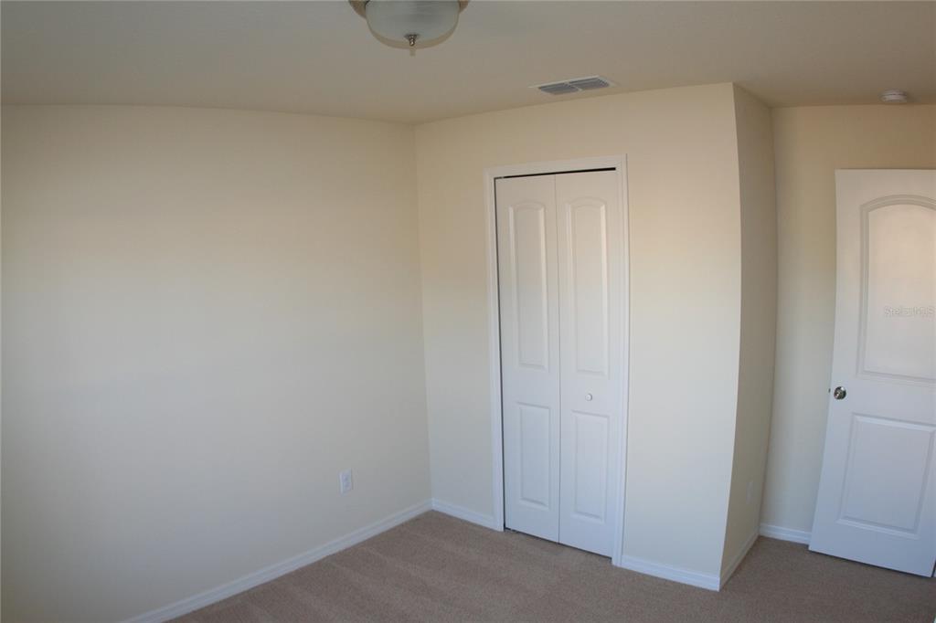 An empty room with beige walls, tan carpeting, a bi-fold closet, and a white door — 4362 HIGH RIDGE AVENUE, SPRING HILL, FL