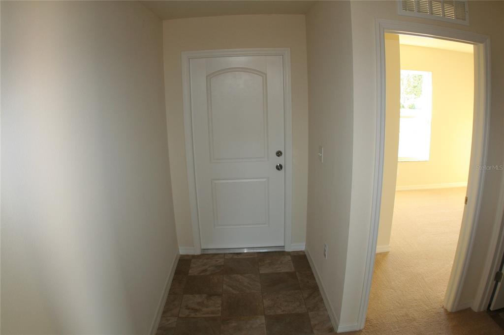 A small entryway with tiled flooring leads to a white front door and carpeted room — 4362 HIGH RIDGE AVENUE, SPRING HILL, FL