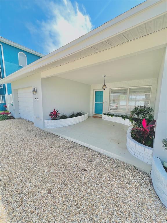 The exterior of a house features a covered porch, white brick planters, and a blue door — 535 173RD AVENUE, NORTH REDINGTON BEACH, FL