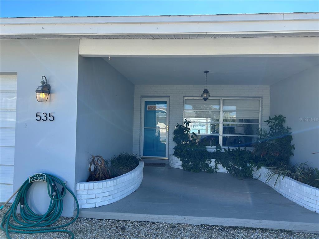 The exterior of a house features a covered porch, a blue front door, and brick planters — 535 173RD AVENUE, NORTH REDINGTON BEACH, FL