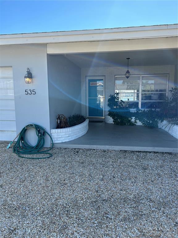 The exterior of a house features a covered entryway, a blue front door, and gravel — 535 173RD AVENUE, NORTH REDINGTON BEACH, FL