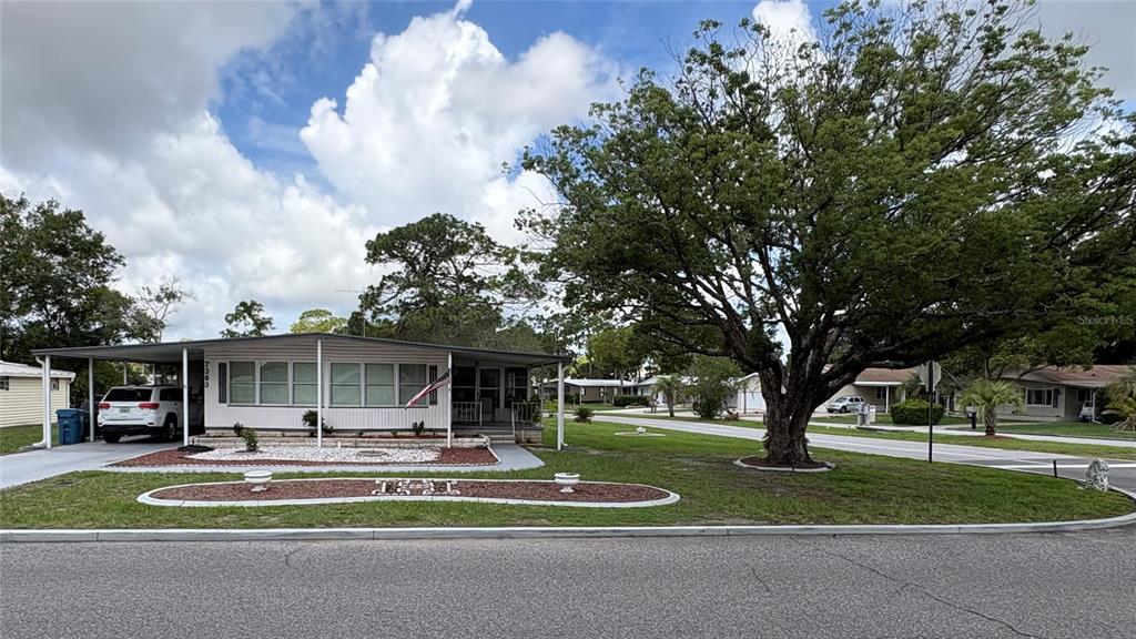 A single-story manufactured home with a carport and a large tree in the front yard — 7363 BROOKRIDGE CENTRAL BOULEVARD, BROOKSVILLE, FL