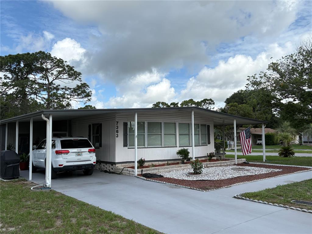 A single-story manufactured home with a carport, white siding, and a gravel front yard — 7363 BROOKRIDGE CENTRAL BOULEVARD, BROOKSVILLE, FL