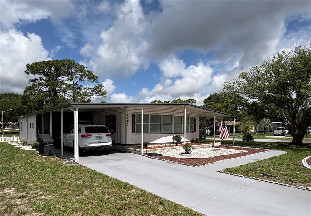 A single-story mobile home with a carport, white siding, and a gravel front yard — 7363 BROOKRIDGE CENTRAL BOULEVARD, BROOKSVILLE, FL