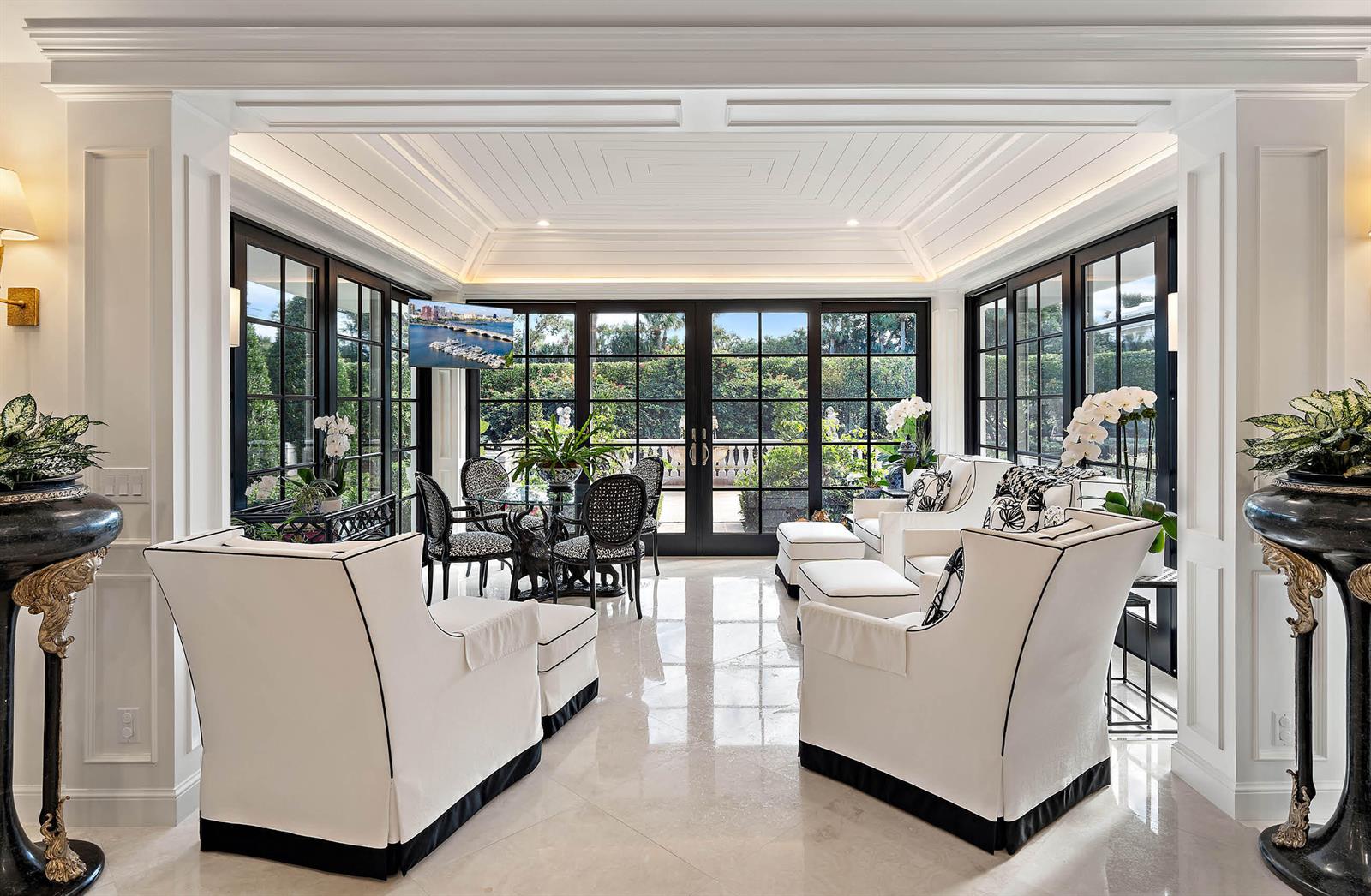 A bright sunroom features white armchairs, a small dining set, and large black-framed windows — 11818 Lost Tree Way, North Palm Beach FL 33408, NORTH PALM BEACH, FL