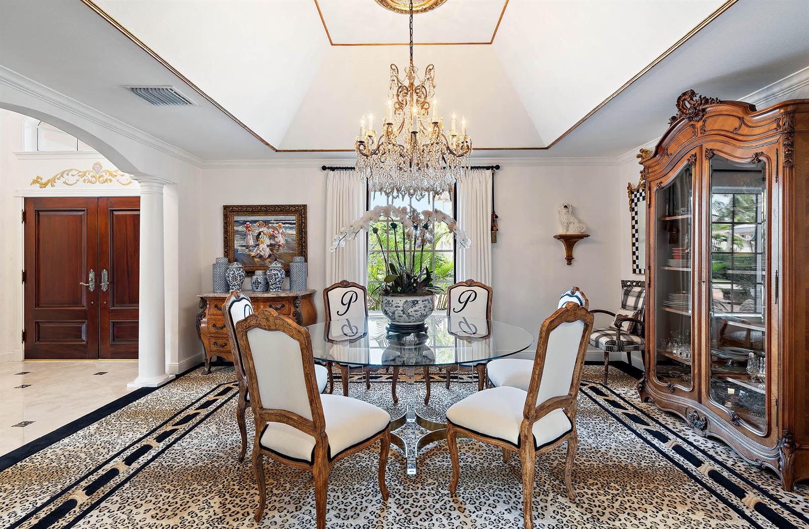 A formal dining room features a glass table, monogrammed chairs, a crystal chandelier, and leopard-print carpet — 11818 Lost Tree Way, North Palm Beach FL 33408, NORTH PALM BEACH, FL