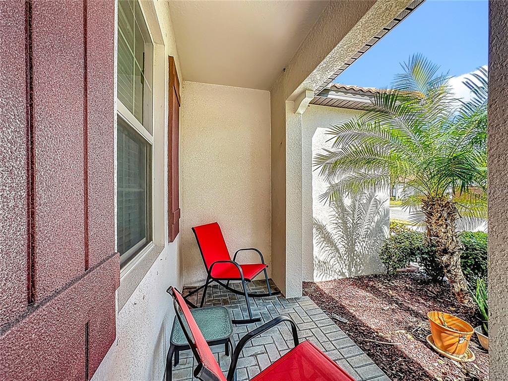 A covered patio features brick pavers, two red rocking chairs, and a small side table — 16815 WHISPER ELM STREET, WIMAUMA, FL