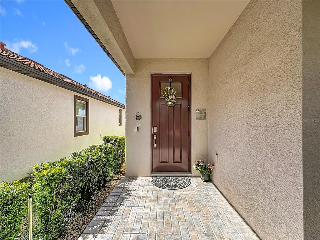 A brown front door with a welcome sign sits under a covered entryway with pavers — 16815 WHISPER ELM STREET, WIMAUMA, FL