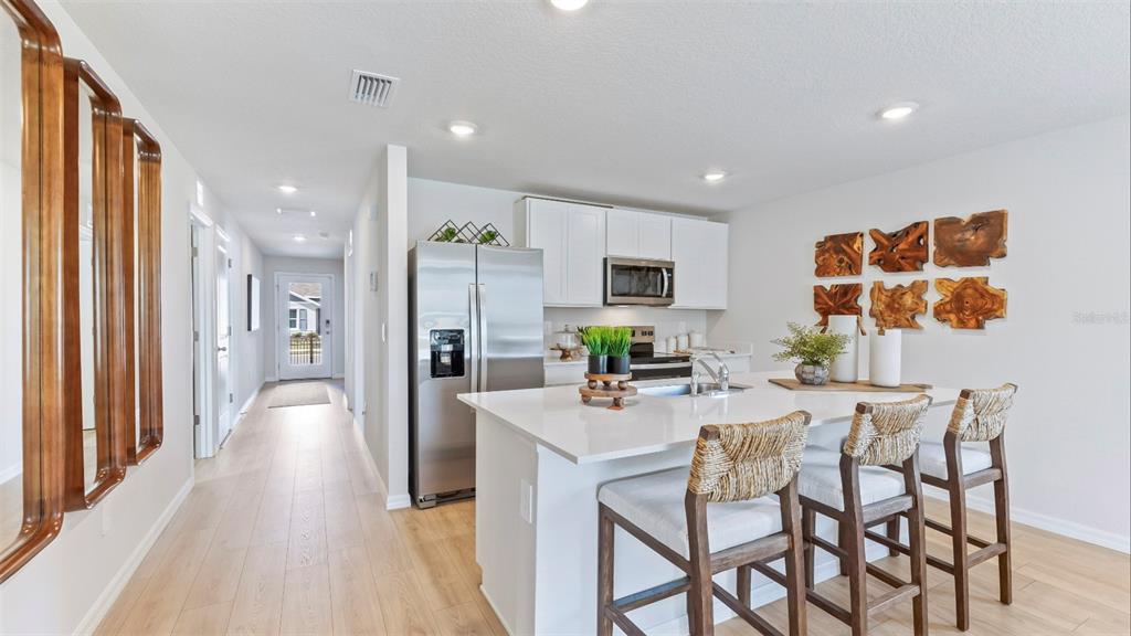 A modern kitchen features white cabinetry, a quartz island with bar stools, and stainless appliances — 13126 OLD CANOE WAY, PARRISH, FL