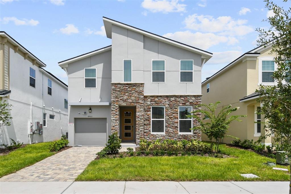 A two-story house with a stone facade, gray stucco, and a single-car garage — 8903 COCONUT BREEZE DRIVE, KISSIMMEE, FL
