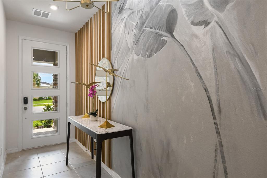 An entryway features a white door, a marble console table, and a large leaf-patterned mural — 8903 COCONUT BREEZE DRIVE, KISSIMMEE, FL