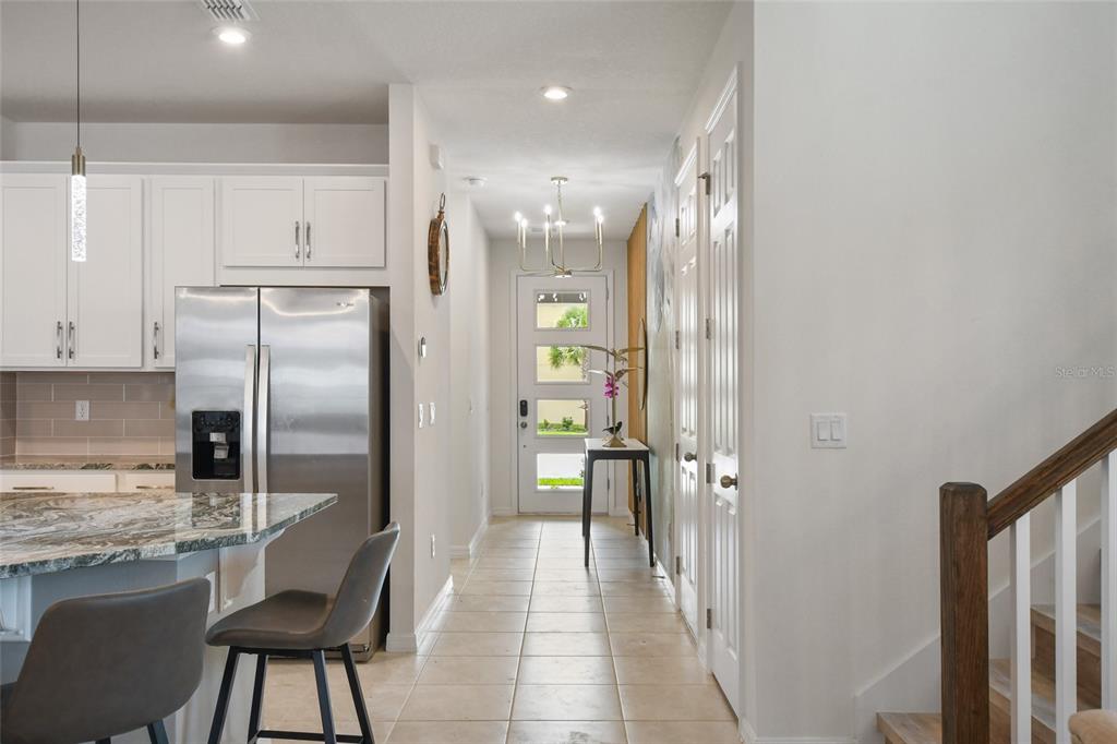 A kitchen with a granite island and stainless steel refrigerator leads to a front entryway — 8903 COCONUT BREEZE DRIVE, KISSIMMEE, FL