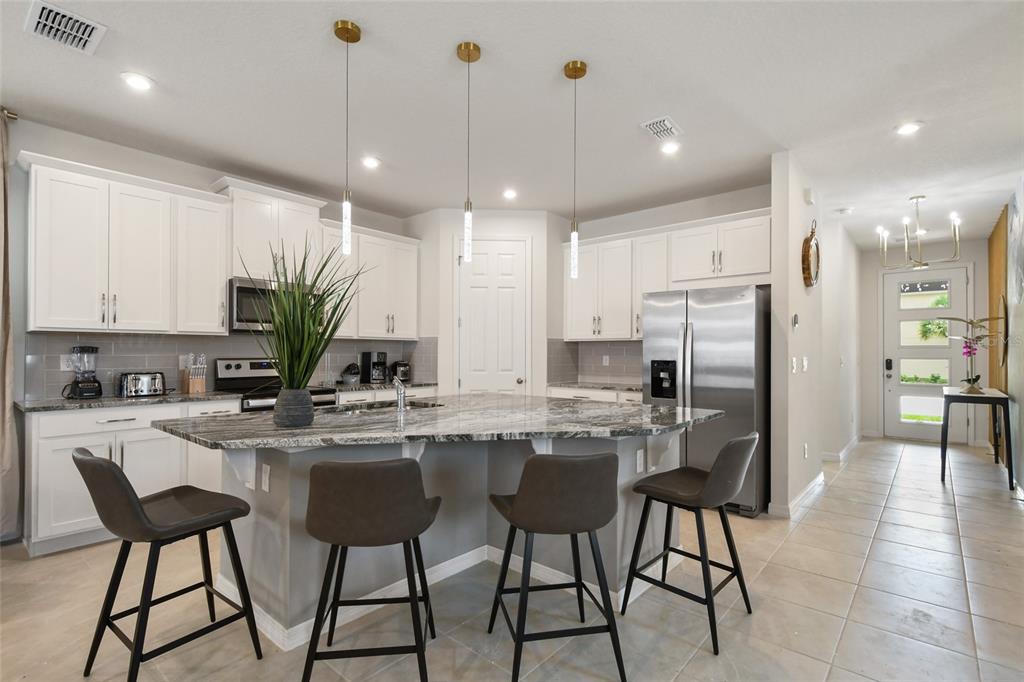 A kitchen features white cabinets, a granite-topped island with four stools, and stainless steel appliances — 8903 COCONUT BREEZE DRIVE, KISSIMMEE, FL