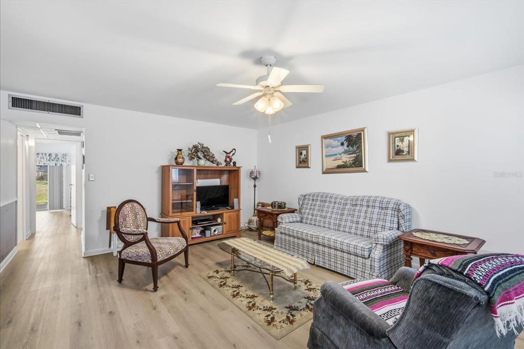 A living room features light wood-look flooring, a plaid sofa, and a ceiling fan — 202 BEDFORD STREET UNIT 49, SUN CITY CENTER, FL