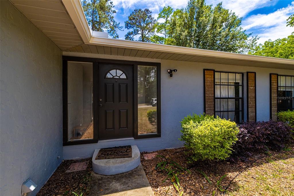 A dark front door with sidelights is centered on the light gray exterior wall — 4607 NW 31ST AVENUE, GAINESVILLE, FL