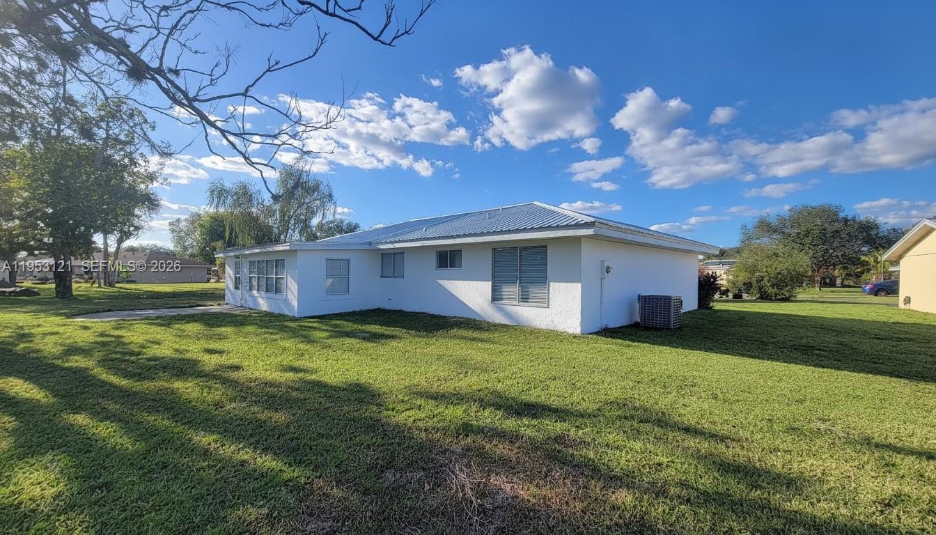 The exterior of a white, single-story house with a metal roof sits on a lawn — 4008 Rye Ct, La Belle FL 33935, LA BELLE, FL