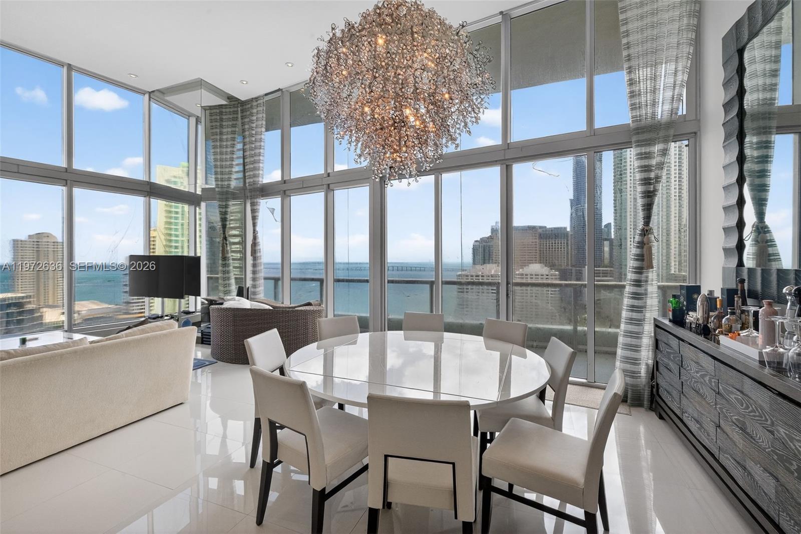A dining area with a round table, chandelier, and floor-to-ceiling windows overlooking the city — 495 Brickell avenue # 2201, Miami FL 33131, MIAMI, FL
