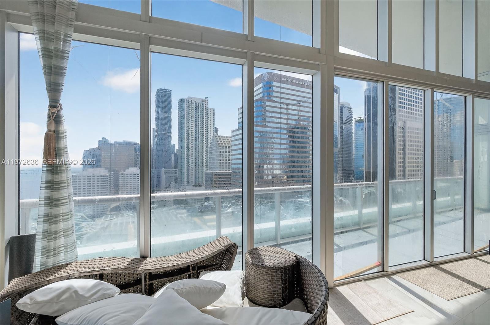 A sunroom with wicker furniture overlooks a dense city skyline through floor-to-ceiling windows — 495 Brickell avenue # 2201, Miami FL 33131, MIAMI, FL