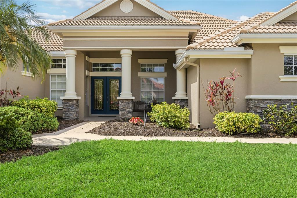 The exterior of a beige house features a covered entryway with columns and stone accents — 5291 WHITE IBIS DRIVE, NORTH PORT, FL
