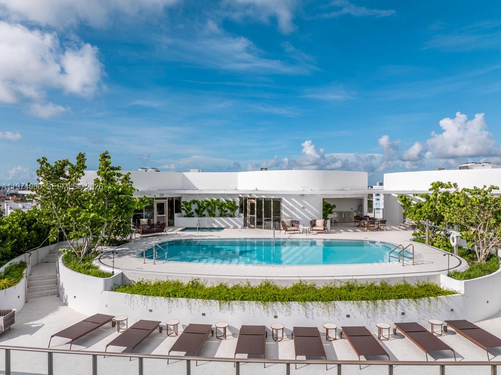 A rooftop swimming pool area features lounge chairs, lush greenery, and a white curved building — 1135 103rd # 307, Bay Harbor Islands FL 33154, BAY HARBOR ISLANDS, FL
