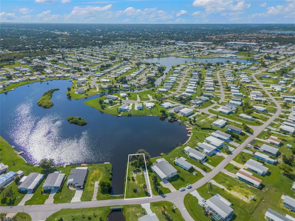 An aerial view shows a vacant residential lot outlined in white next to a lake — 1329 BLUE HERON DRIVE, ENGLEWOOD, FL