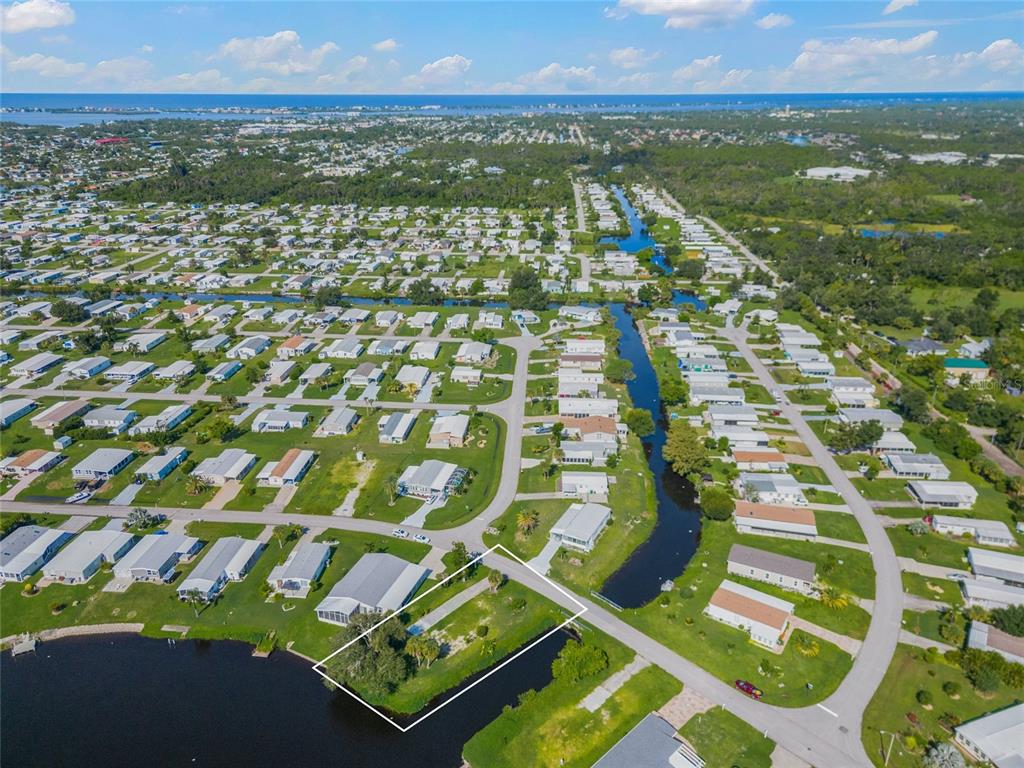 An aerial view shows a vacant, grassy waterfront lot outlined in white within a residential neighborhood — 1329 BLUE HERON DRIVE, ENGLEWOOD, FL