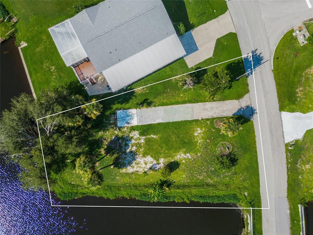 An aerial view shows a vacant waterfront lot with a concrete driveway and surrounding vegetation — 1329 BLUE HERON DRIVE, ENGLEWOOD, FL