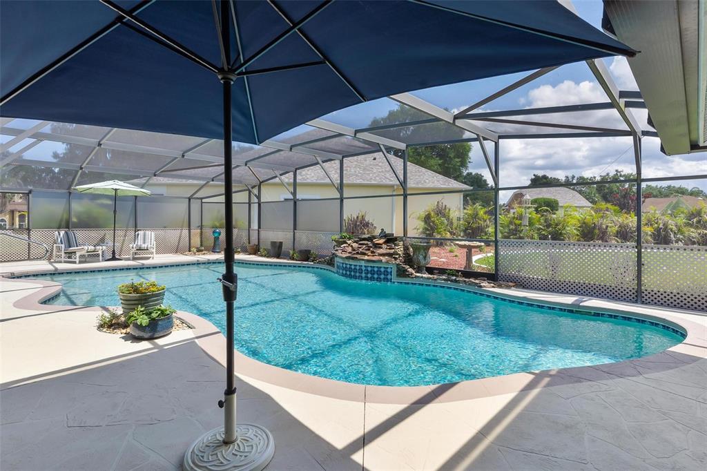 A screened-in swimming pool features a rock waterfall and a patio with an umbrella — 26515 SAVAGE CIRCLE, HOWEY IN THE HILLS, FL