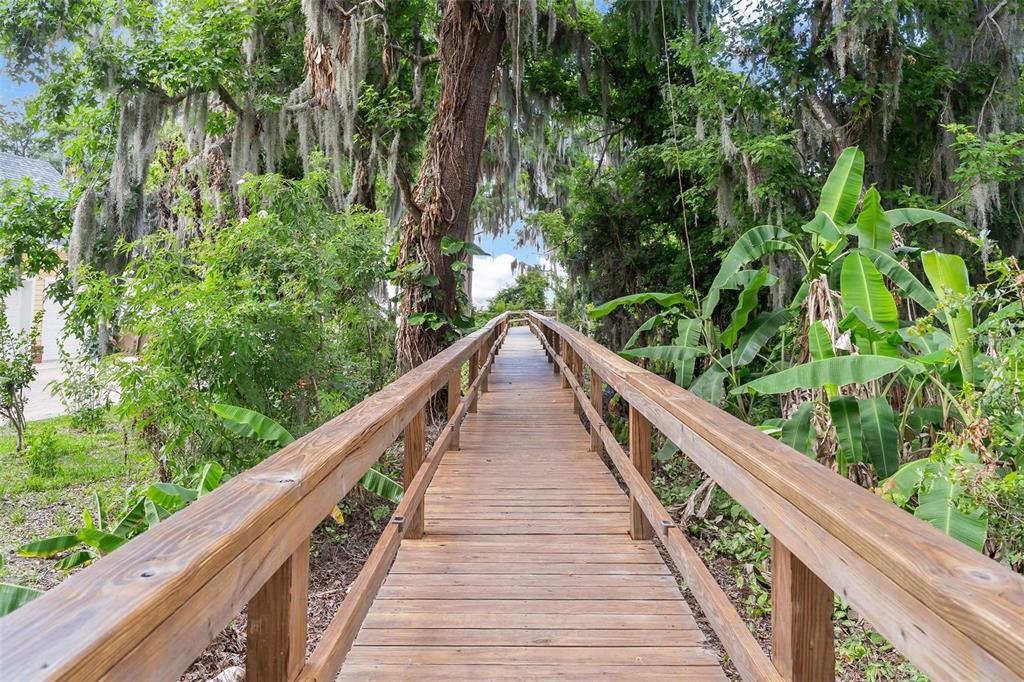 A wooden boardwalk leads through a lush, tree-lined area with hanging moss and tropical plants — 26515 SAVAGE CIRCLE, HOWEY IN THE HILLS, FL