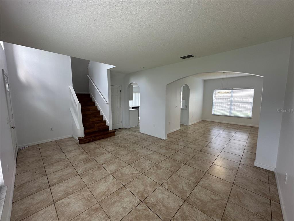 An open-concept room features tiled floors, a wooden staircase, and arched entryways — 747 PELICAN COURT, POINCIANA, FL