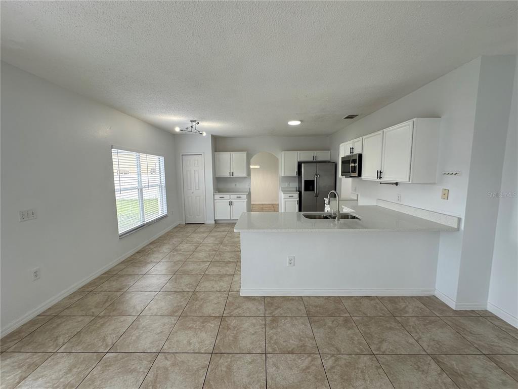 A kitchen with white cabinets, a breakfast bar, and tile flooring opens to a dining area — 747 PELICAN COURT, POINCIANA, FL