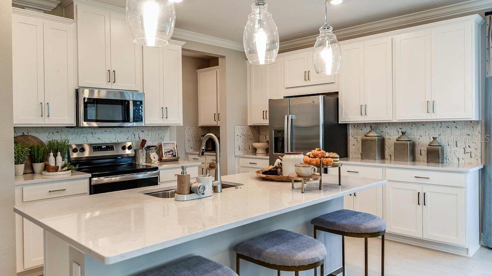 A modern kitchen features white cabinets, a large quartz island, and stainless steel appliances — 25 GEOSAM DRIVE, PALM COAST, FL